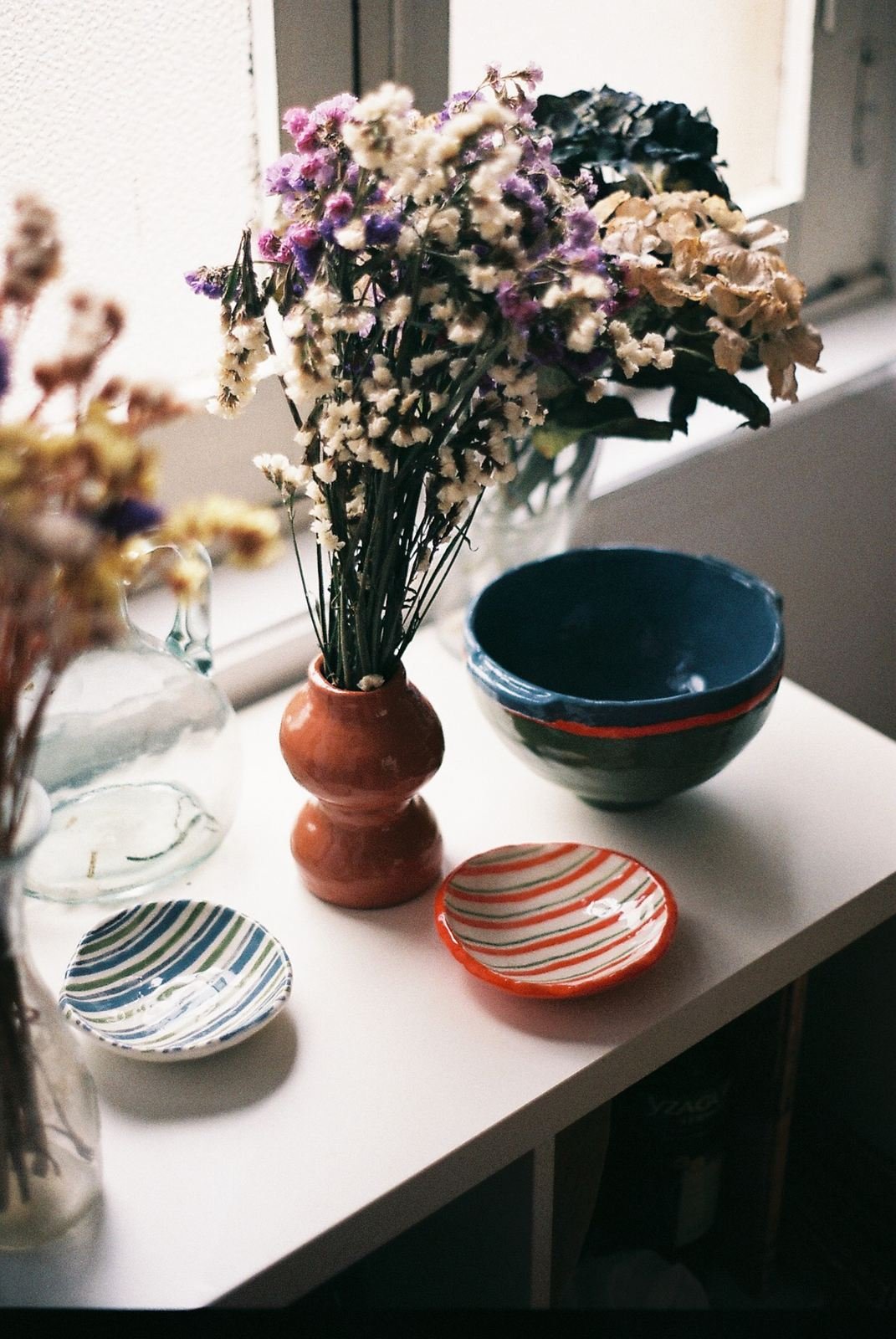 «Cerámica mecánica» de Toin: florero de barro con flores secas, cuenco azul y platillos de rayas pintados a mano
