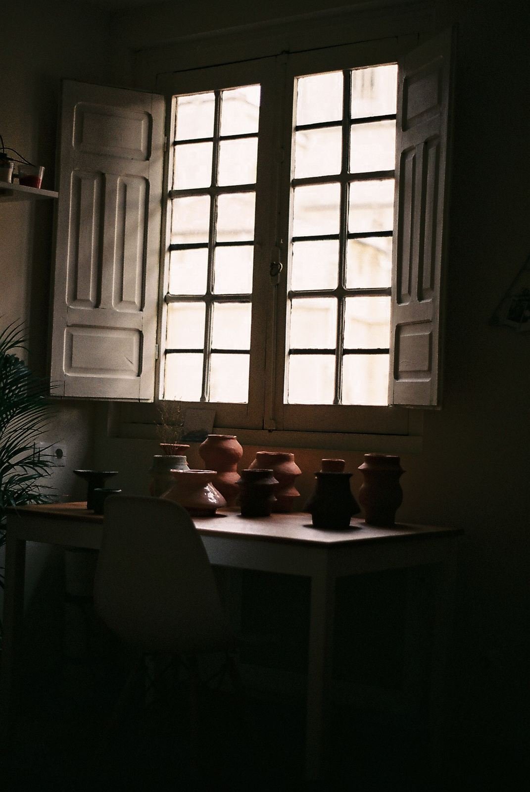 «Cerámica mecánica» de Toin: piezas de barro sobre una mesa, a contraluz de una ventana con contraventanas blancas