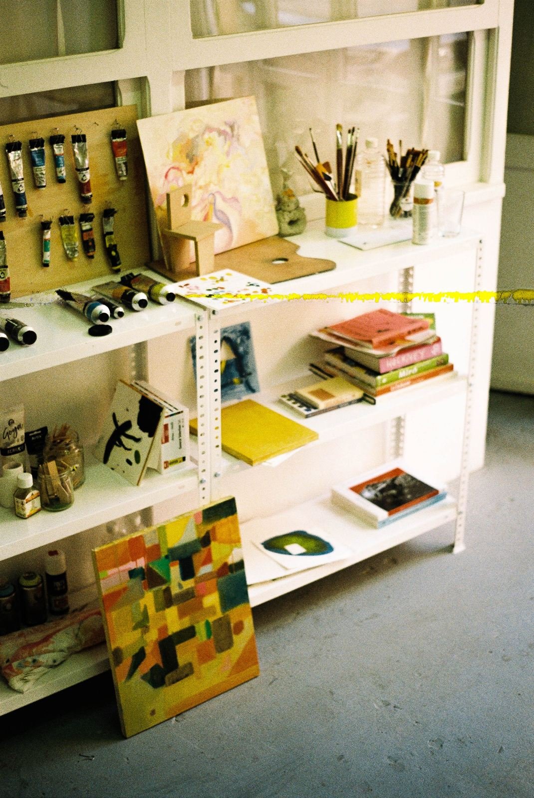 Estudio de Lucía Zamudio: estantería con tubos de óleo, pinceles, libros y pequeños cuadros