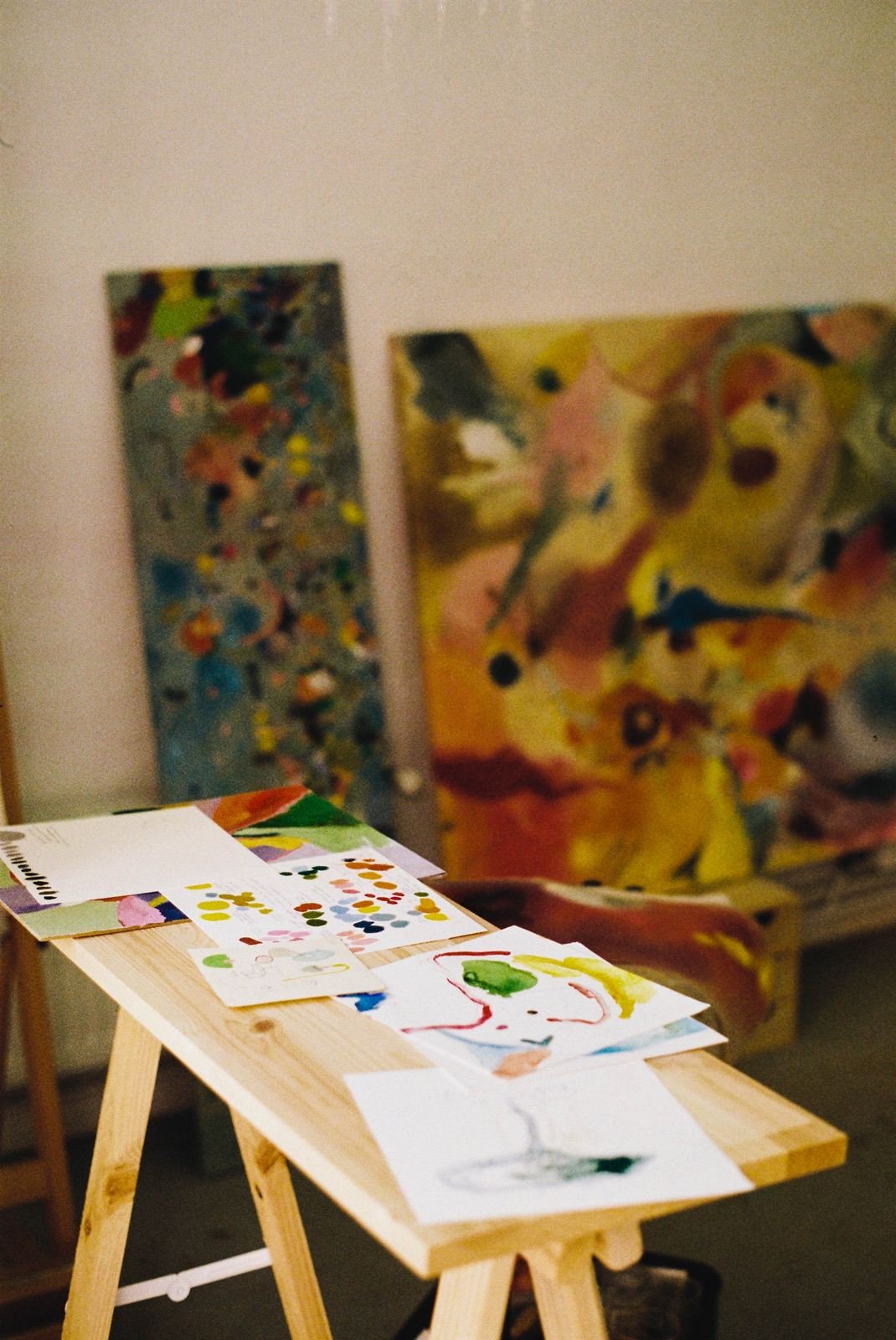 Estudio de Lucía Zamudio: bocetos y muestras de color sobre un tablero, con dos lienzos grandes al fondo
